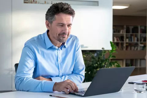 Mann sitzt lächelnd vor Laptop