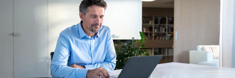Mann sitzt lächelnd vor Laptop